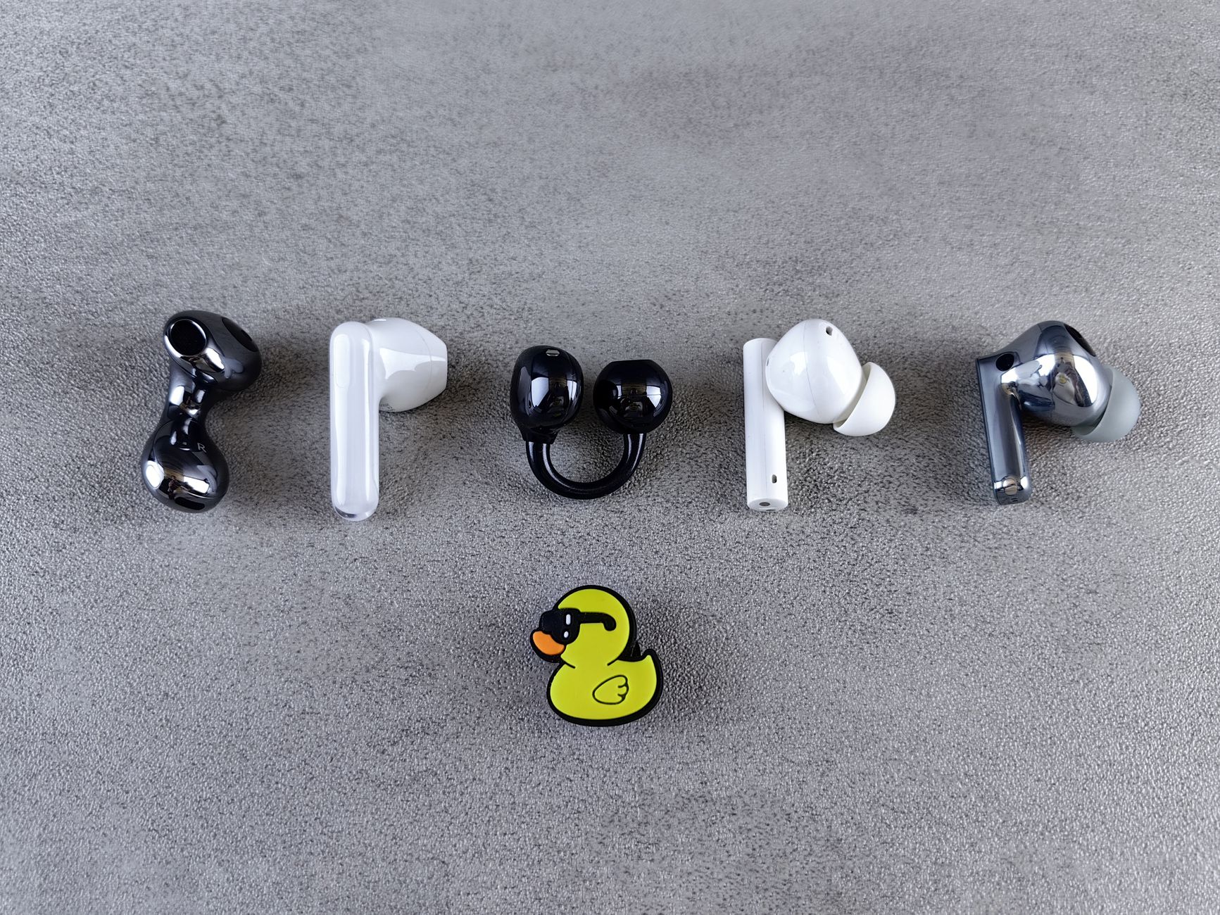 Stylish wireless earbuds creatively arranged with a playful rubber duck on gray background.