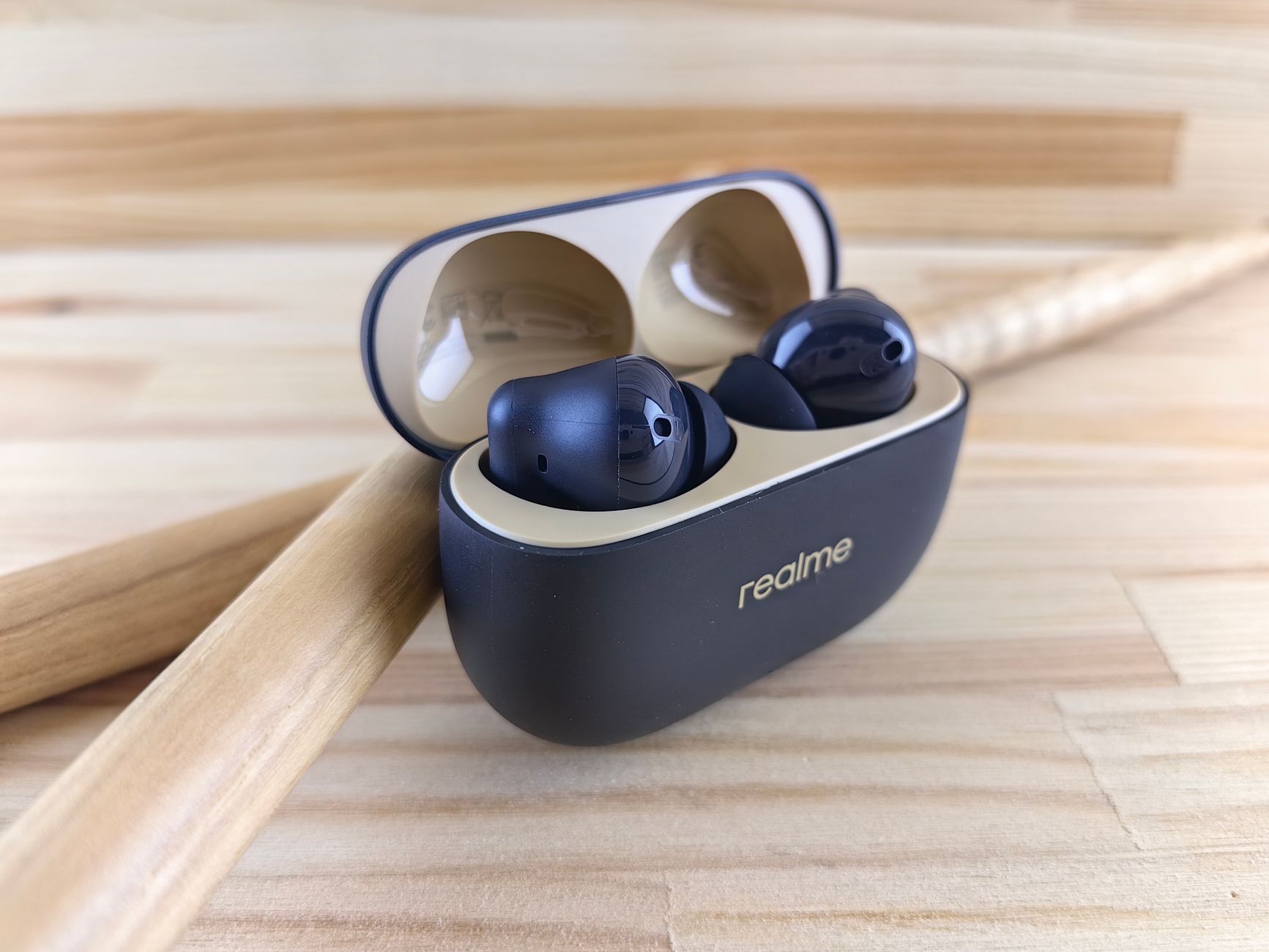 Modern Realme wireless earbuds in a sleek case on a wooden background, combining style and tech.