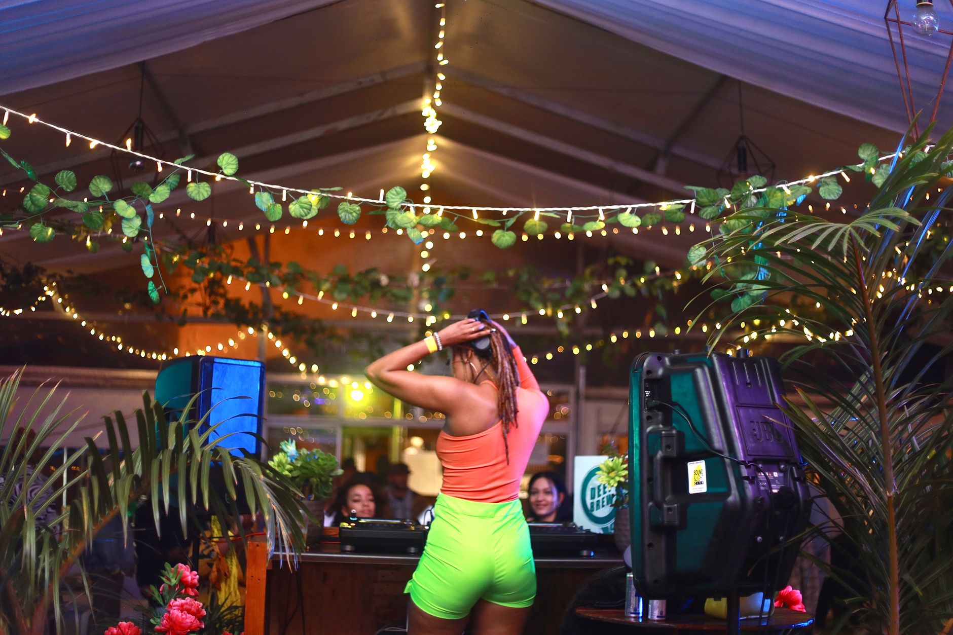 A DJ energizes the crowd at an indoor summer party with colorful lighting and lively decor.