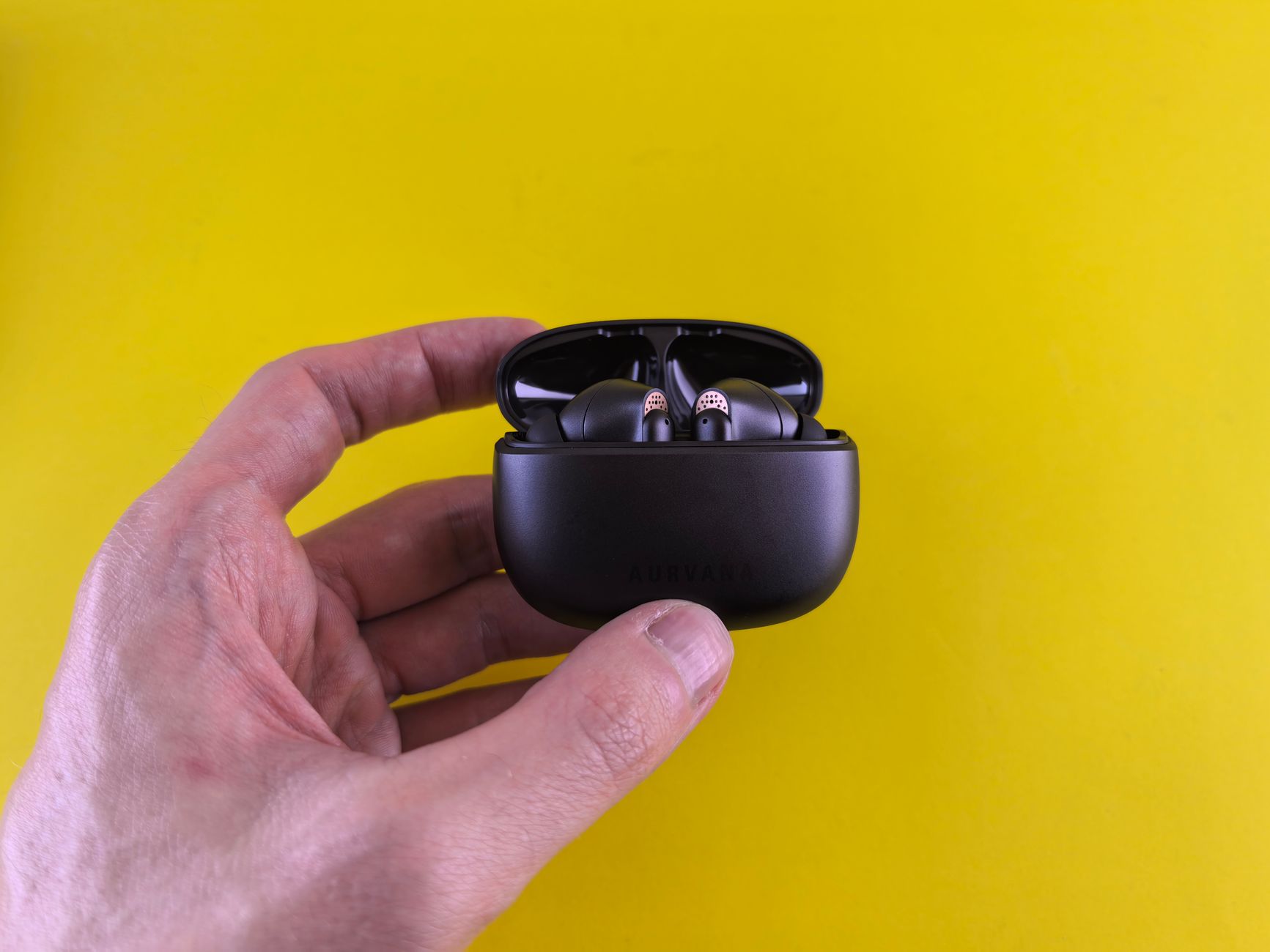 Sleek black wireless earbuds in a charging case held against a vibrant yellow background.