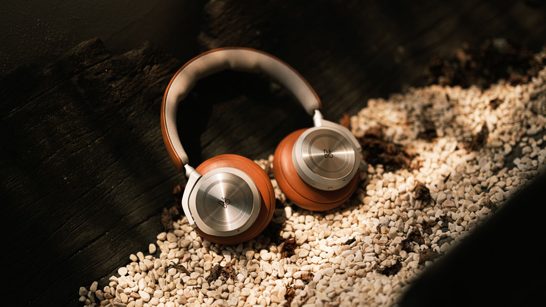 Elegant leather headphones resting on a bed of white pebbles in bright sunlight, exuding luxury and style.