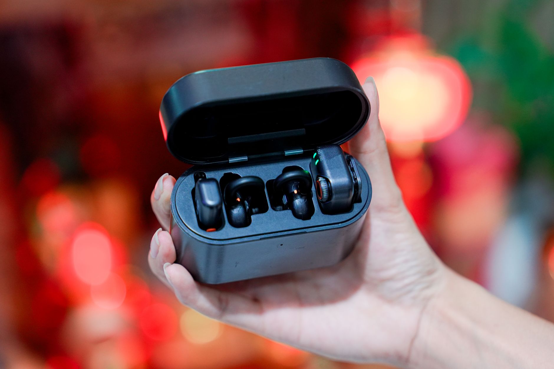 A hand holds a pair of black wireless earbuds in an open charging case.