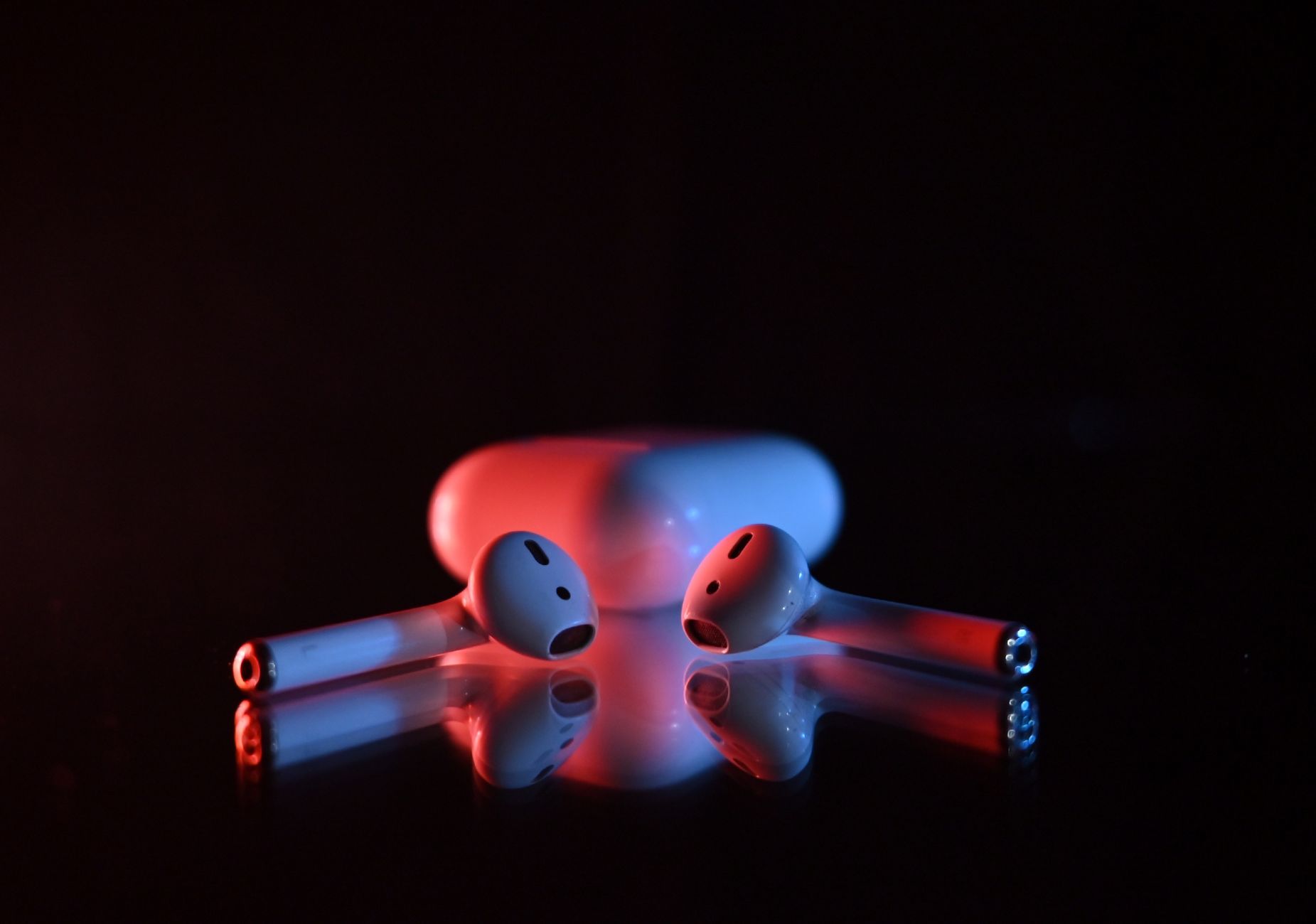 Wireless earbuds in a dramatic red and blue lighting on a reflective surface.