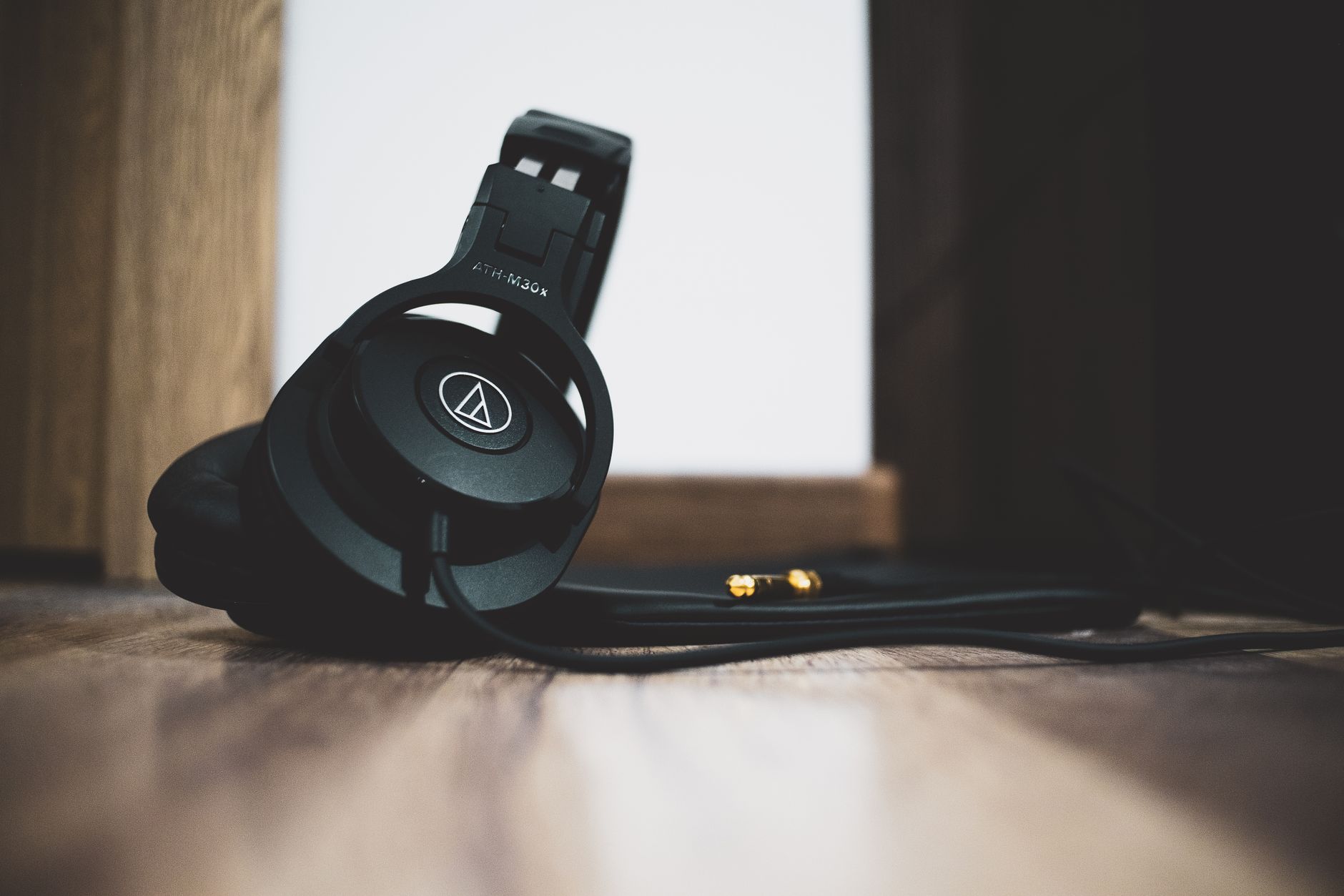 Stylish black headphones with cable lying on a wooden floor in a low-angle shot.