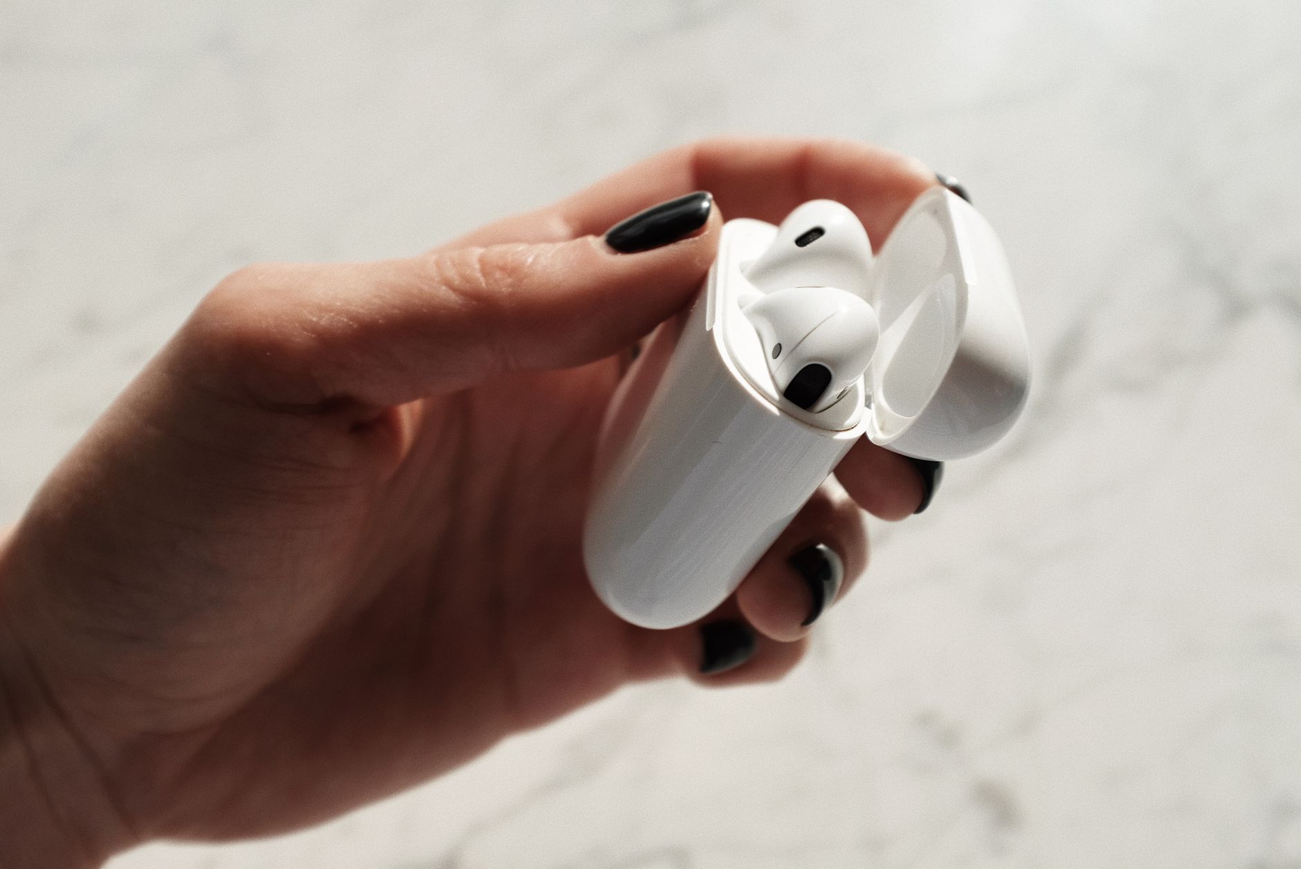 Close-up shot of a hand holding wireless earphones with a marble background.