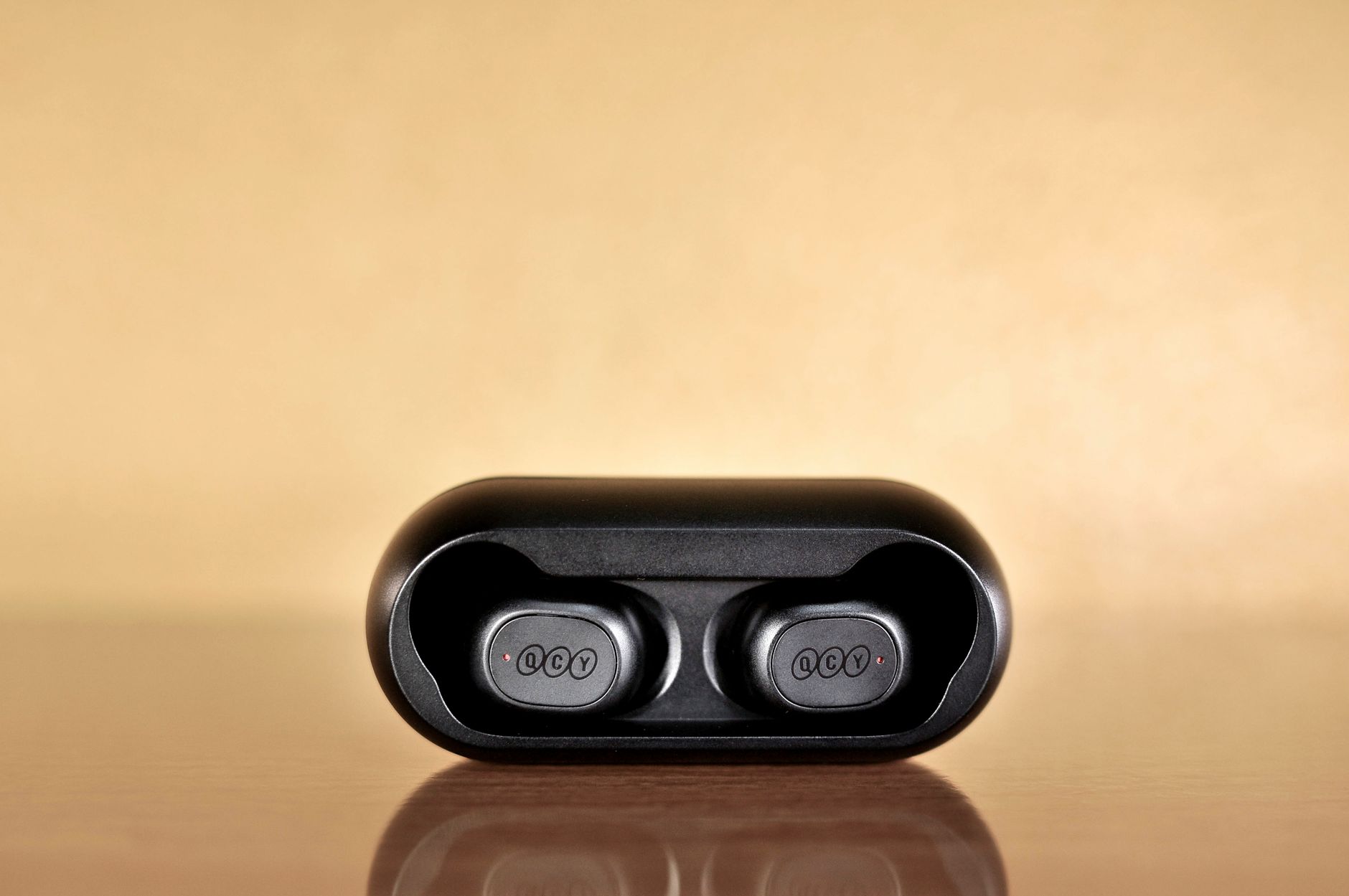 Black wireless Bluetooth earbuds in a case against a warm, reflective background.